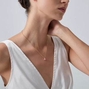 Woman wearing a delicate gold necklace with a pink pendant on a plain background