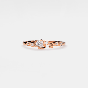 Rose gold ring with a heart-shaped center stone on a white background