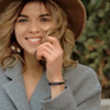 A couple wears matching black braided bracelets with gold bars. The man takes a photo of the woman in a hat, and the video ends with them holding hands and smiling.