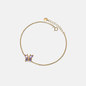 Gold bracelet with a butterfly charm on a light beige background