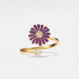 Gold ring with purple floral design and embedded diamonds on a light gray background