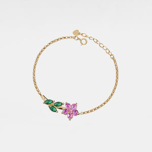 Gold bracelet with pink and green gemstones on a light gray background