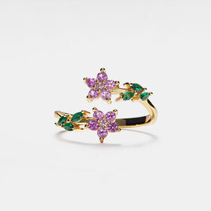 Gold ring with pink and green gemstone flowers on a white background
