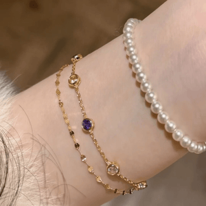 Gold bracelet with gemstones and pearl bracelet on a wrist against a neutral background