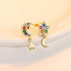 Gold earrings with star and moon designs and colorful gemstones on a soft background.