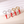 Four pairs of earrings with red chili pepper charms on a light pink background