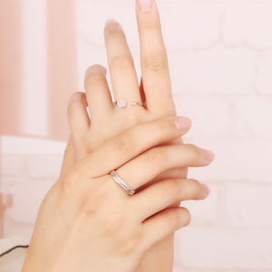 Hand wearing two silver rings on a soft pink background
