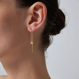 Gold chain earring worn by a person with a neutral background