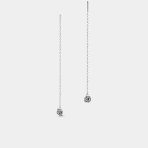 Silver rose-shaped earrings on thin chains against a white background