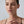 Close-up of a woman wearing long, thin earrings against a neutral background