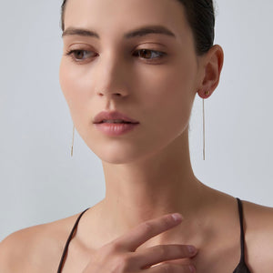 Close-up of a woman wearing long, thin earrings against a neutral background