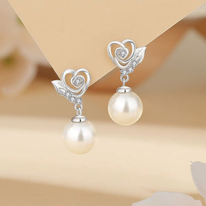Pearl earrings with silver heart and leaf designs on a beige background