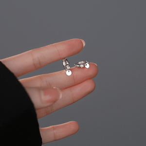Two silver earrings held between fingers against a gray background