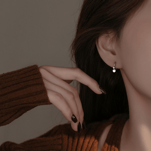 Close-up of a person wearing a silver earring with a pearl, against a neutral background.