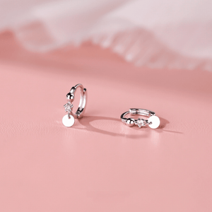 Pair of silver hoop earrings with round pendants on a pink background