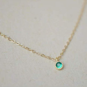 Gold necklace with a green gemstone on a light background