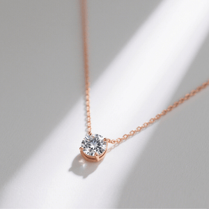 Rose gold necklace with a diamond pendant on a light gray background