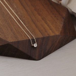 Gold necklace with a small round pendant on a wooden surface