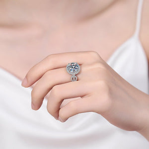 Close-up of a hand wearing a silver ring with a large gemstone on a plain background
