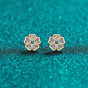 Gold flower-shaped earrings with clear stones on a teal glittery background