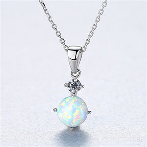 Two round opal charm necklaces with gold plating on a white background, one with a blue opal and the other with a white opal, both on silver chains.