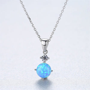 Two round opal charm necklaces with gold plating on a white background, one with a blue opal and the other with a white opal, both on silver chains.