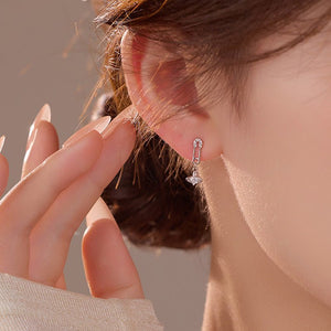 Close-up of a person wearing a silver earring with a clear gemstone.