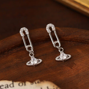 Silver safety pin earrings with clear gemstones on a wooden surface