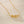 Gold necklace with shell, pearl, and starfish charms on a beige textured background