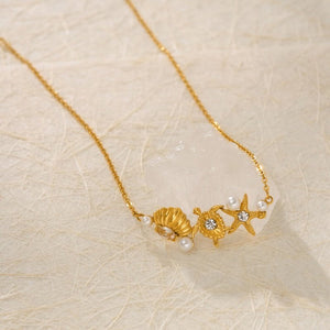 Gold necklace with shell, pearl, and starfish charms on a beige textured background