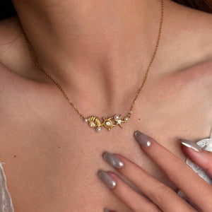 Gold necklace with shell and pearl details worn by a person