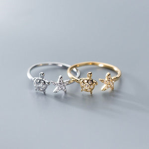 Two turtle-shaped rings, one gold and one silver, on a gray background.