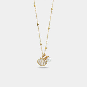 Gold necklace with a shell and pearl pendant on a light gray background