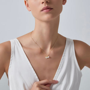 Woman wearing a white sleeveless top and gold necklace with a pendant on a light gray background