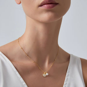Gold necklace with a pendant worn by a person on a plain background