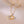 Two necklaces, one with a silver shell-shaped pendant and the other with a gold shell-shaped pendant, both with pearl details, displayed on a beige background.