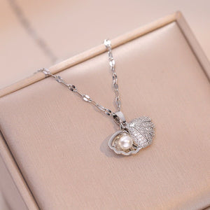Two necklaces, one with a silver shell-shaped pendant and the other with a gold shell-shaped pendant, both with pearl details, displayed on a beige background.