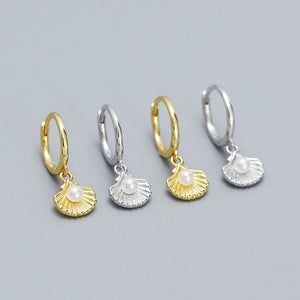Pair of gold and silver hoop earrings with shell and pearl charms on a gray background