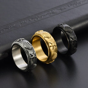 Three spinner rings, one gold, one silver, and one black with starfish and shell designs on a dark textured surface.