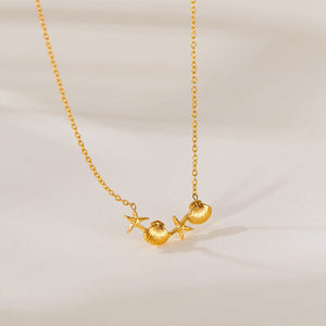 Gold necklace with shell and starfish pendants on a beige background