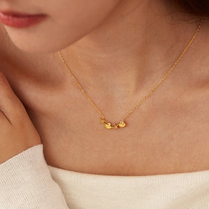 Gold necklace with heart-shaped pendants on a person wearing a white top.