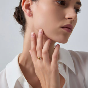 Woman wearing a gold ring starfish and shell design on her finger against a neutral background