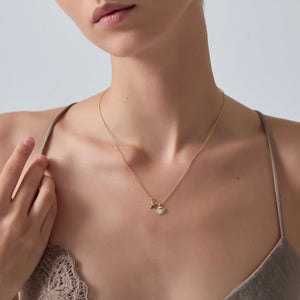 Woman wearing a delicate gold necklace with a small pendant on a plain background