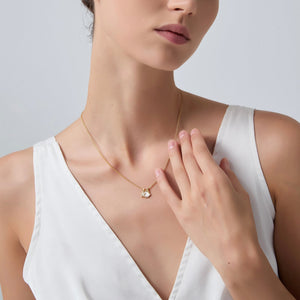 Woman wearing a gold necklace with a heart pendant on a plain background