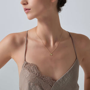 Woman wearing a gold necklace with a green pendant on a plain background