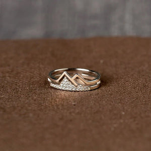 A silver band ring with a mountain-like design and small cubic zirconia embellishments on the top surface, set against a blue background.