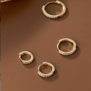 Gold hoop earrings with embedded stones on a brown surface