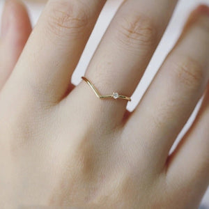 Gold ring with a small diamond on a person's finger against a neutral background