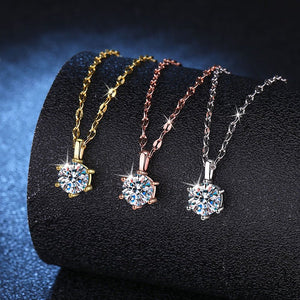 Three diamond pendants on chains in gold, rose gold, and silver on a black stand.