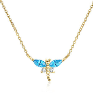 A small blue dragonfly pendant necklace on a gold-plated chain, displayed on a person's neck.